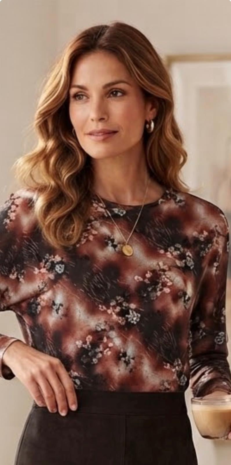A woman wearing a long-sleeve crewneck blouse with a brown, black, and beige floral and abstract pattern, paired with a dark skirt.